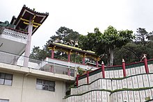 On top of walls a Chinese arch with dragons and a bell. On the walls, there is Chinese writing.