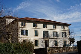 Vue d’une maison de deux étages, avec cinq fenêtres aux volets verts par étage.