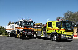 ACT Rural Fire Service CAFS tanker and an ACT Fire Brigade pumper. Scania 94D 260 truck (yellow) and Isuzu truck (white). Both with "FIRE" in mirror writing ("ERIF").