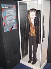 Un manteau en cuir, une chemise à fleurs, un pantalon noir et des chaussures noires exposés en vitrine.