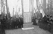 Cérémonie militaire autour d'un monument avec civils et officiels. Grands arbres.