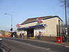 A white-bricked building with a dark blue, rectangular sign reading "LEYTON STATION" in white letters all under a blue sky fading to purple on the horizon