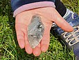 Der Dolch von Gessel liegt in einer Hand, die das Fundstück in Bodennähe über einem Rasen präsentiert, rechts ist ein Turnschuh zu sehen