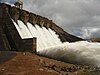 Water rushes over a concrete structure blocking a river.