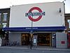 A light grey building with a sign stating "ARSENAL STATION" in white letters on a blue background and four bicycles laying idle in the foreground