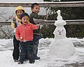 Barn i Huanglong i Sichuan i Kina med snømann med utklipte andletstrekk og tradisjonelt lokalt hovudplagg utforma i snø.