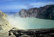 A photograph depicting a blue sky with white clouds at the top, a light grey lake in the middle, and dark grey rocks surrounding the lake.