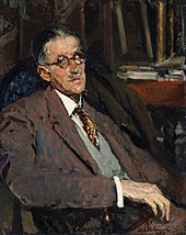 seated portrait of James Joyce in a suit. He is in three-quarters view looking left, wearing a suit. Table with books is in background on the right.