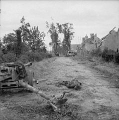 Un canon antichar allemand de 75 mm hors service et l'un de ses artilleurs gisant mort à côté de lui. Un char Panther désactivé et un Marder IIIM sont également visibles en arrière-plan, 25 juin 1944 (opération Martlet)