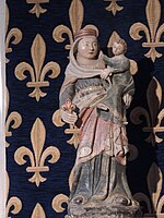 Photographie d'une statue polychrome de la Vierge, présentée devant une tenture bleue à fleur-de-lys.