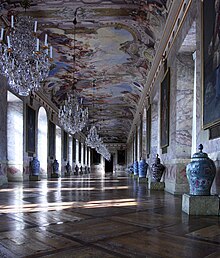 A view down the Ahnengalerie. The walls, made of scagliola, are lined with portraits of the rulers of Württemberg, their arms, and an urn. Above the gallery is a massive fresco, featuring several Classical figures, glorifying the reign of Eberardo Luis.