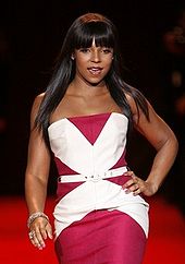 A woman wearing a red and white-patterned dress; peoples' faces can be seen in the background.