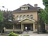 A two-storey brick house with a roofed porch standing in a park