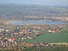 Barevná fotografie zalesněné a z části osídlené krajiny v jejímž středu se nachází jezero Olbersdorf