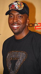 Headshot of a man wearing a black T-shirt and a black cap