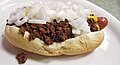 A hot dog sausage topped with beef chili, white onions and mustard