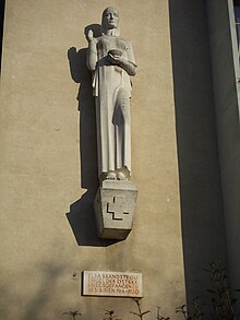 Lebensgroße Figur aus Sandstein. Emblem des Roten Kreuzes als Relief auf dem Sockel.