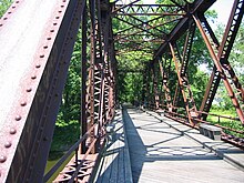 A photo (taken in daytime) of some of a bridge which is near vegetation