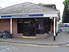 A red-bricked building with a rectangular, dark blue sign reading "WOODFORD STATION" in white letters all under a clear, white sky