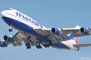 A large white and blue four-engine jet airliner with union tail fin, with landing gear extended