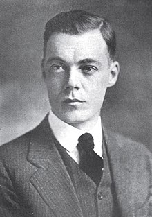 A young, dark-haired man wearing a black jacket, vest, and tie and a white shirt