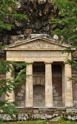 Le portique du Rocher vue de face. Derrière les colonnes, une niche en voûte en plein cintre en pierre claire. Des rochers de grès du rocher surplombent le portique.