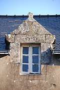 Photographie d'une lucarne au fronton triangulaire, sur fond de toit en ardoise.