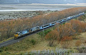 Blue train on single track surrounded by trees near a river