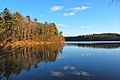 A late fall sunny day shows the pond's blue waters and tree-lined shores.