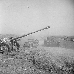 Tank dan jip Britania Raya melewati meriam yang ditinggalkan Jerman, 8 Agustus 1944.