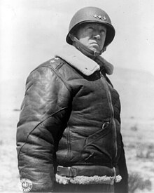 Photo en noir et blanc représentant le buste d'un homme vêtu d'un casque surmonté de trois étoiles et d'un blouson d'aviateur.