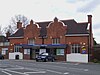 A brown-bricked building with a black roof and a blue sign that reads "CHIGWELL STATION" in white letters all under a white sky