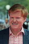 A red-headed white man wearing a white-and-red-striped shirt smiling towards the camera.