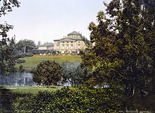 photographie couleurs : un bâtiment vu à travers un parc (arbres et lac)