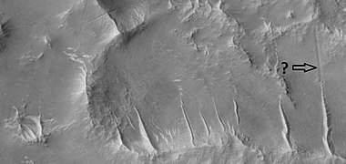 Close view of ridges and possible faults that are visible as straight lines, as seen by HiRISE under HiWish program. Arrow points to a narrow trough that lines up with a ridge.