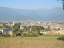 Small rural houses behind some brown grass against a mountain backdrop; A view of Surkhet valley from Latikoili