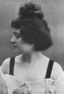 A young woman in profile, with light skin and abundant dark hair piled on top of her head; she is wearing a lowcut white gown with wide dark shoulder straps