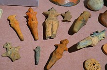 Nine human-shaped figurines on a table surrounded by other artefacts