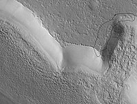 O manto cobre a maior parte dessa área. Observe a ausência de rochas na face do penhasco. Uma área que mostra as bordas do manto é circundada. Região do Quadrângulo de Ismenius Lacus. Imagem fotografada pela Mars Global Surveyor.