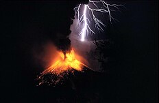 A photograph depicting a white bolt of lightning with a purple aura striking a volcano as it erupts yellow lava with a red aura and black smoke.