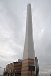 Ground-level view of a tall, white, angular chimney rising from a brown, striped building