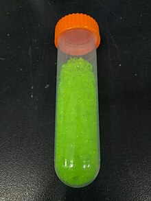 yellowish green crystals in a transparent vial with an orange ribbed screw on cap