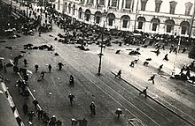 Panikařící dav demonstrantů rozprchávající se po široké ulici kvůli střelbě.