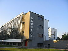 Un grand bâtiment moderne, à la géométrie stricte, marqué des lettres du mot Bauhaus sur un pignon.