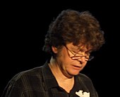 Middle-aged man with brown hair, wearing eyeglasses and a dark shirt, while reading a book