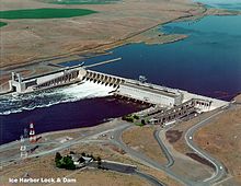 Aerial view of a concrete dam on a river surrounded by rolling hills and farmland