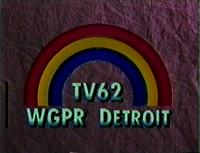 On a dark purple textured background, a rainbow consisting of three colors—blue, yellow, and red, from inside to outside. Beneath the rainbow is the text "TV62 / WGPR DETROIT" in a light green.