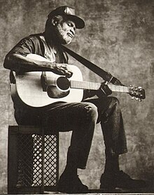 Hawkins seated on a milk crate, playing guitar