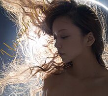 A blue-tinted close-up face shot of a woman, with long hair being windswept to her right. In the background is an extreme close-up of an annular solar eclipse.