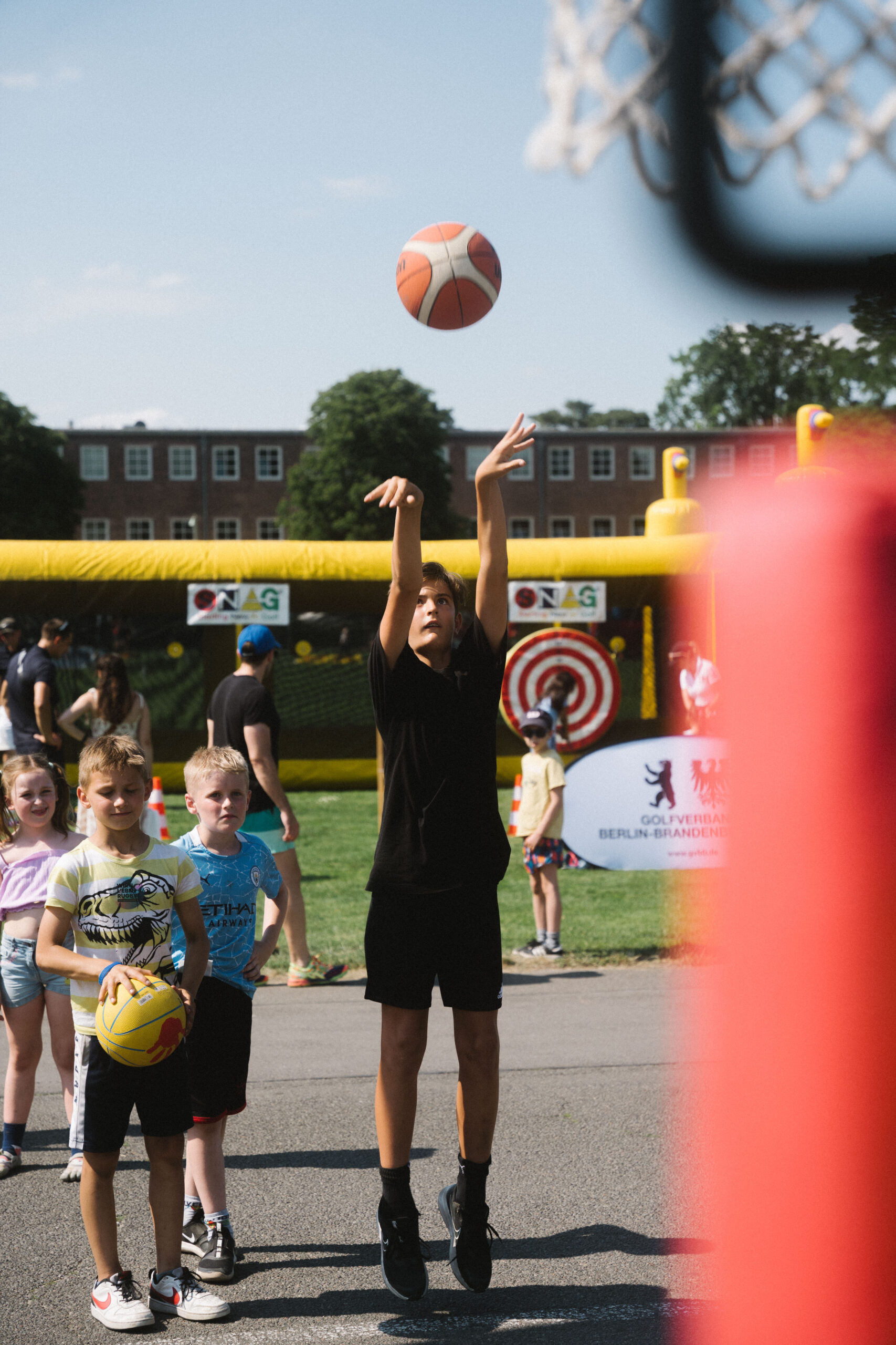 Junge wirft auf einen Ball in den Korb und Kinder stehen an